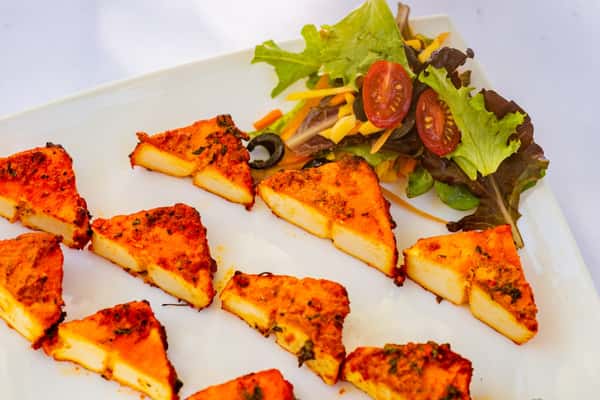Tandoori paneer triangles—grilled Indian cottage cheese marinated in spiced yogurt—served with a side of fresh salad greens, cherry tomatoes, shredded carrots, and black olives.