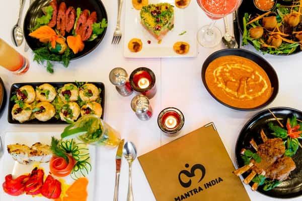 Colorful spread of Indian cuisine at Mantra India, featuring curries, appetizers, grilled meats, drinks, and festive garnishes.