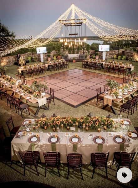 large outdoor wedding reception setup with banquet tables, floral arrangements, and a central dance floor under string lights