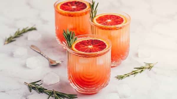 Three glasses of pink grapefruit cocktails with a blood orange slice and rosemary sprig garnish.