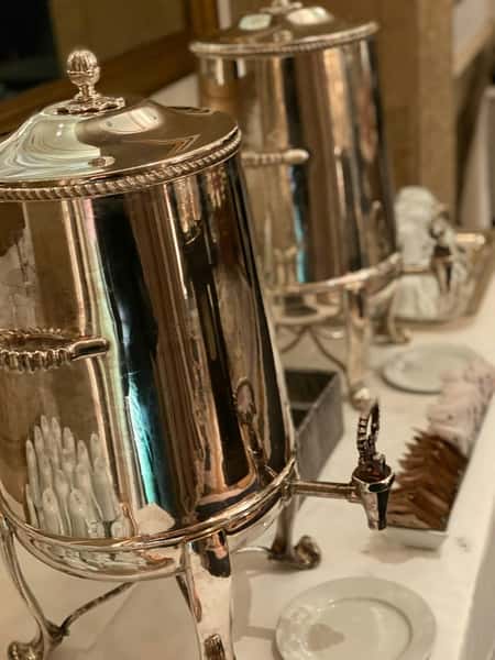 Polished silver beverage dispensers set on a white tablecloth, likely for serving hot drinks like tea or coffee at a formal event.