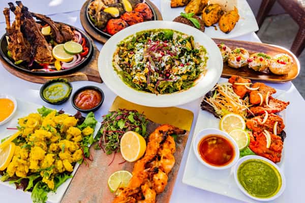 Colorful Indian feast with tandoori lamb, shrimp, calamari, spinach chaat, fish pakora, and dahi puri served with chutneys.