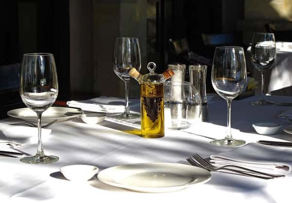 Elegant outdoor dining table set with wine glasses, plates, cutlery, and a decorative oil and vinegar cruet in the sunlight.
