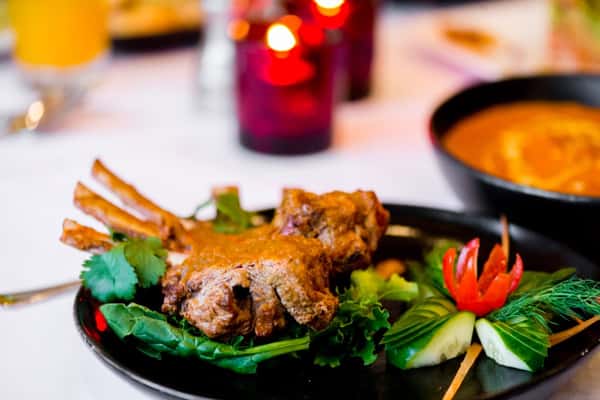 Tandoori lamb chops served on a bed of greens with cucumber and tomato garnish, lit by soft candlelight.