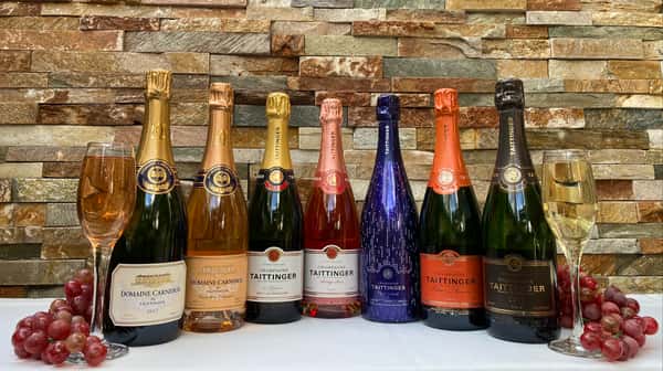 A row of a variety of champagne on a table with a glass of champagne on both ends