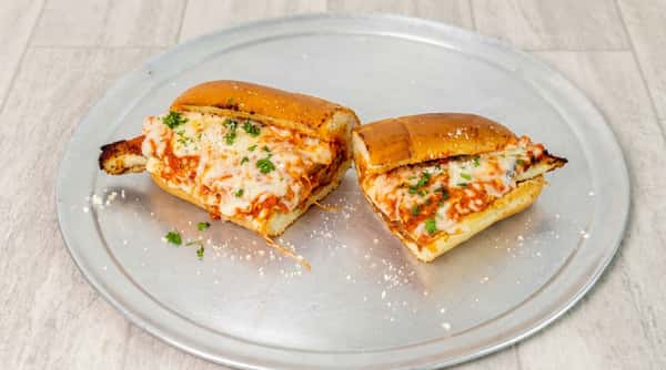 Chicken parmesan hero, cut in half, with melted mozzarella, marinara, parmesan, and parsley on a metal tray.