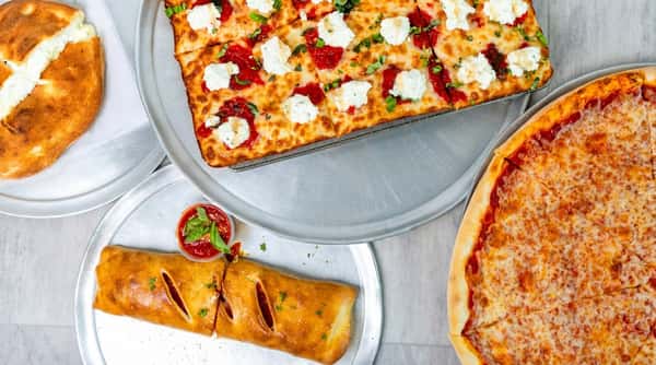 A top-down view of various Italian dishes: a whole cheese pizza, a square pizza with ricotta and tomato sauce, and a Stromboli.