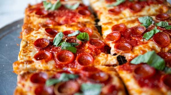 Close-up of square-cut pepperoni pizza slices with melted cheese and fresh basil leaves.