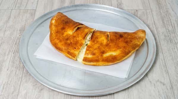 Golden-brown calzone, sliced to show melted cheese and filling, on white parchment paper on a metal pizza pan.