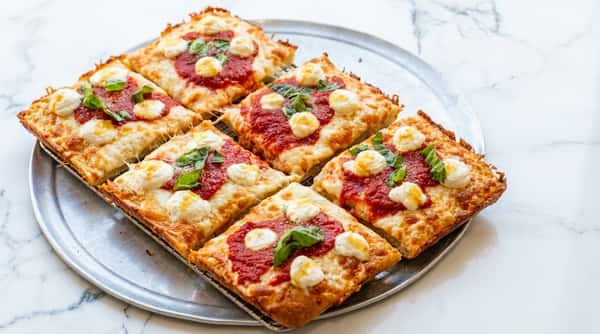 Sicilian pizza slices with tomato sauce, mozzarella, ricotta cheese dots, and basil on a silver platter.
