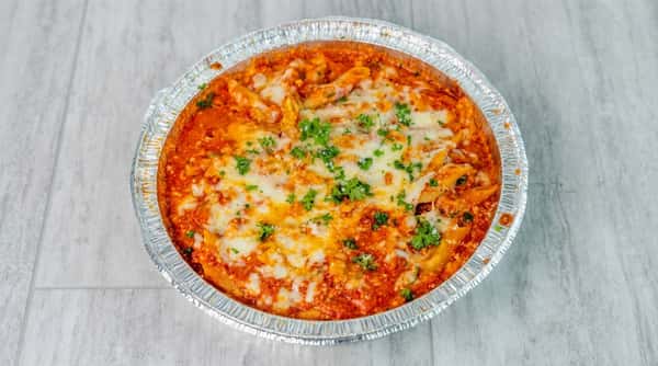 Baked ziti with penne pasta, red sauce, melted mozzarella, and fresh parsley in an aluminum pan.
