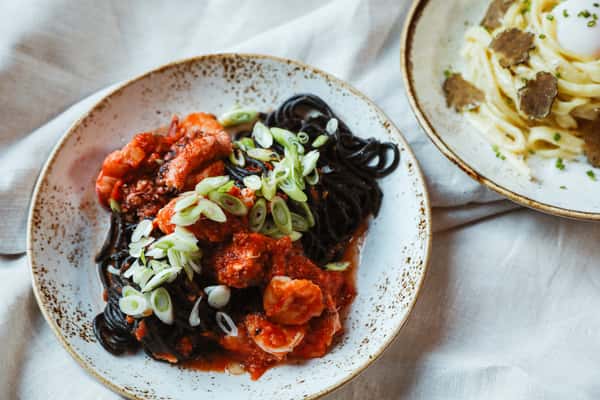 Italian entree showcasing vibrant red, green, and black colors presented on a white plate set against a pristine white tablecloth.