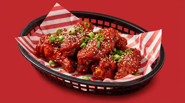 Spicy fried chicken wings coated in red sauce, topped with sesame seeds and chopped green onions in a basket