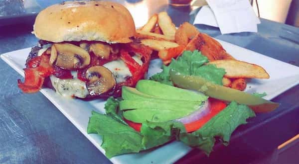 hamburger topped with mushrooms with lettuce, tomato and fries on the side