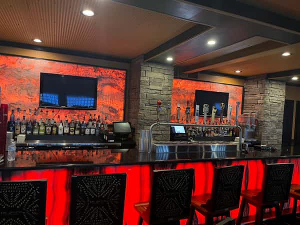The image shows a bar area with liquor bottles, a black countertop, and red backlit panels. This picture is likely used to add visual interest on the restaurant's "About" page.
