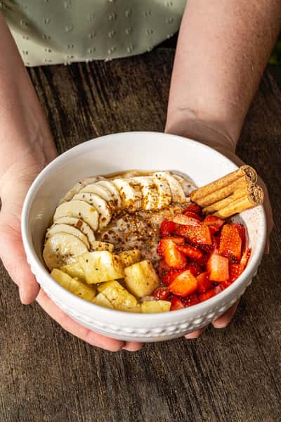 Oatmeal bowl topped with banana slices, pineapple chunks, strawberries, and cinnamon sticks on a rustic wooden table.