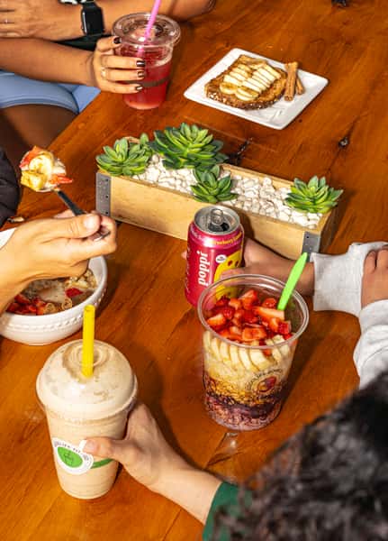 Group enjoying smoothies, acai bowls, toast, and soda at a wooden table with a succulent centerpiece at Good Life Nutrition.