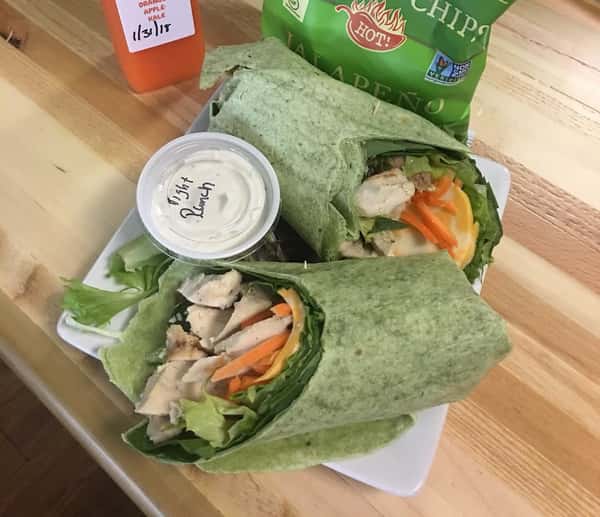 Spinach wraps filled with grilled chicken, lettuce, cheese, and carrots, served with light ranch, chips, and a bottled juice.