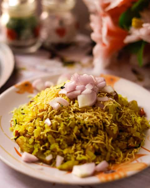 Indian poha topped with sev and finely chopped onions, served on a floral-patterned plate with a blurred floral background.