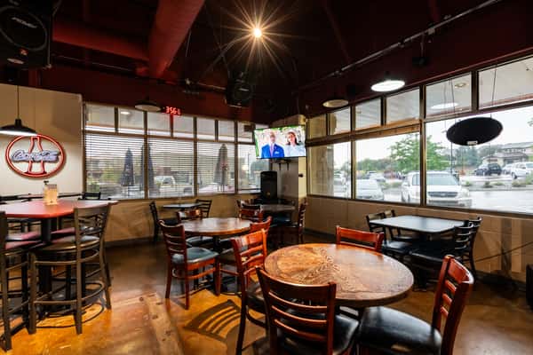 Spacious dining area at Parkway Tavern featuring high-top tables, large windows with blinds, warm ambient lighting, and sports-themed décor, creating a relaxed and inviting atmosphere.