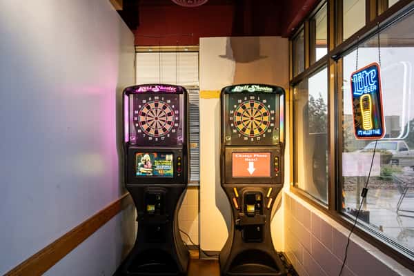 Two illuminated Bull Shooter electronic dartboards at Parkway Tavern, positioned in a cozy corner with neon signs and large windows, creating a fun and casual bar game atmosphere.