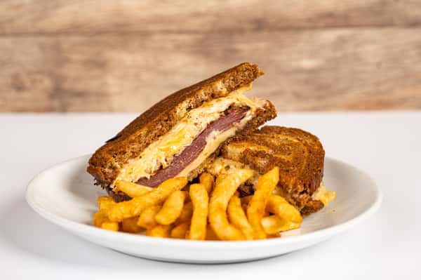 Close-up of a juicy patty melt sandwich stuffed with grilled mushrooms, melted cheese, and beef on crispy toasted rye bread, served with golden French fries on a white plate.