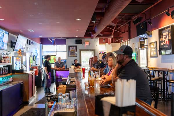 Lively interior of Parkway Tavern with patrons seated along a polished wooden bar, enjoying drinks and conversation in a sports-themed setting with framed jerseys and neon lights.