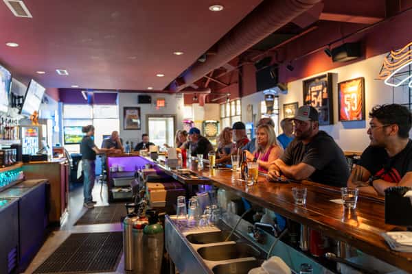 Lively interior of Parkway Tavern with patrons seated along a polished wooden bar, enjoying drinks and conversation in a sports-themed setting with framed jerseys and neon lights.