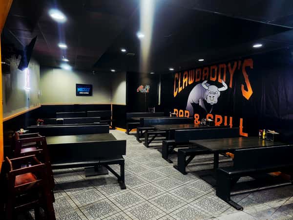 Restaurant seating area with dark benches and a large Clawdaddy's Bar & Grill mural on the wall.