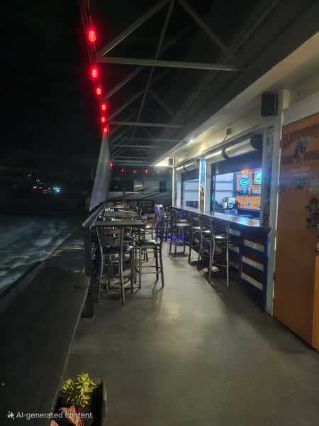 Outdoor bar seating area at night with high tables, red string lights, and view into the interior bar.