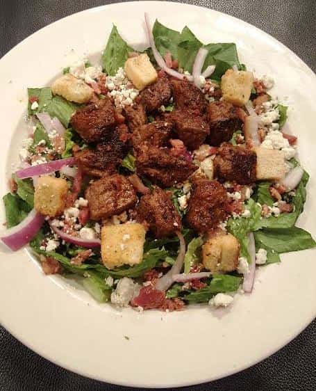 Black and Bleu Steak Salad. Cajun seasoned sirloin, bacon, red onions, and bleu cheese crumbles over a crisp bed of romaine or spring mix.
