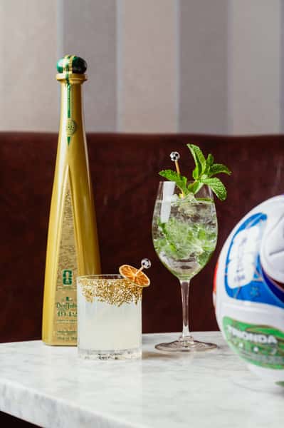a bottle of Don Julio with cocktails made from it and a soccer ball