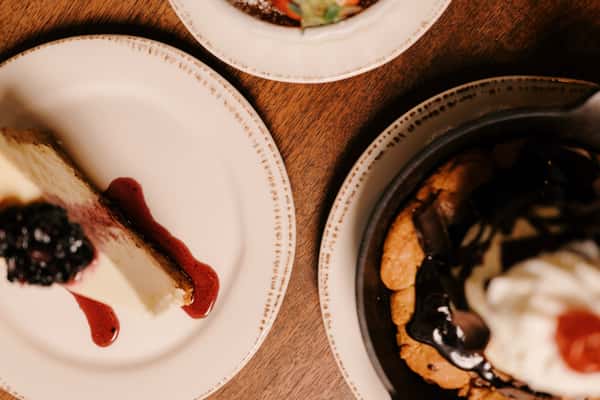 Overhead view of cheesecake with berry sauce, chocolate chip skillet cookie with whipped cream, and crème brûlée with strawberry.