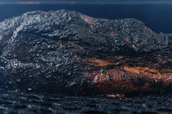 Close-up of a smoked brisket with a dark, bark-covered crust and juicy marbling, fresh off the barbecue pit.
