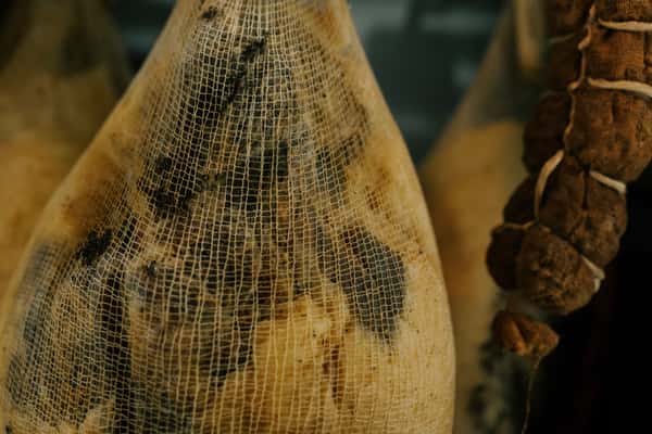 Close-up of aged cured meats wrapped in cheesecloth, showcasing the traditional dry-aging process in a charcuterie environment.