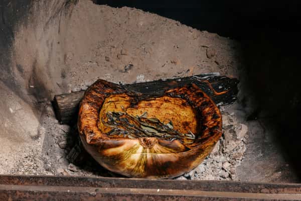 Roasted squash with herbs and charred edges cooking directly over wood and ashes in an open-fire oven.
