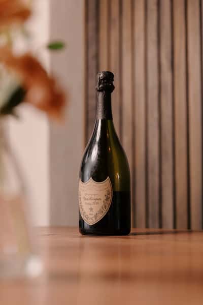 Bottle of Dom Pérignon Vintage 2013 champagne displayed on a wooden table with a softly blurred floral arrangement in the foreground.