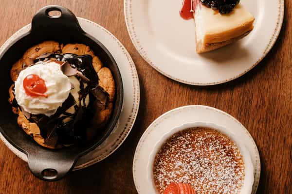 Trio of desserts featuring skillet cookie with ice cream, berry-topped cheesecake slice, and crème brûlée garnished with sliced strawberry.
