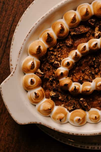 Sweet potato casserole topped with toasted marshmallow swirls and pecan crumble, served in a white ceramic baking dish.