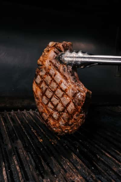 Grilled steak held with tongs showing perfect diamond sear marks on the hot grill.