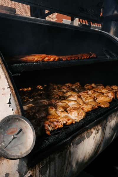 Smoked chicken pieces and ribs cooking inside a large metal barbecue smoker with a temperature gauge on the side.