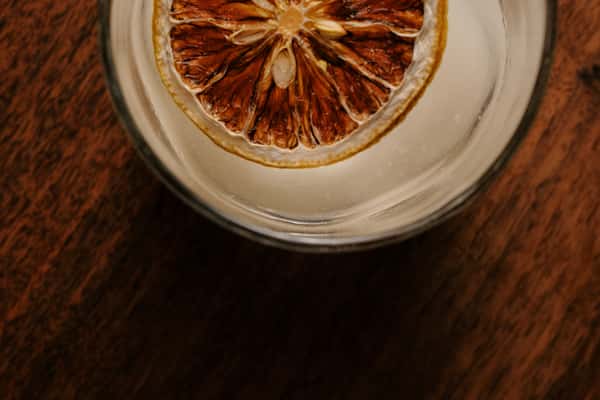 Craft cocktail served over ice and garnished with a dried citrus wheel in a clear glass on a wooden table.