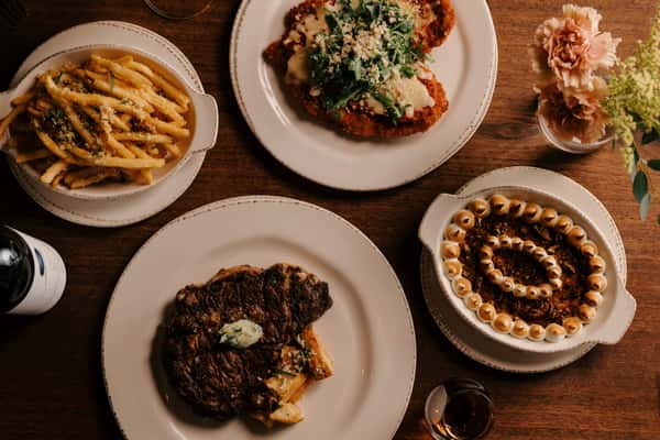 Upscale dinner spread with grilled ribeye, truffle fries, sweet potato casserole, and chicken parmesan topped with arugula.