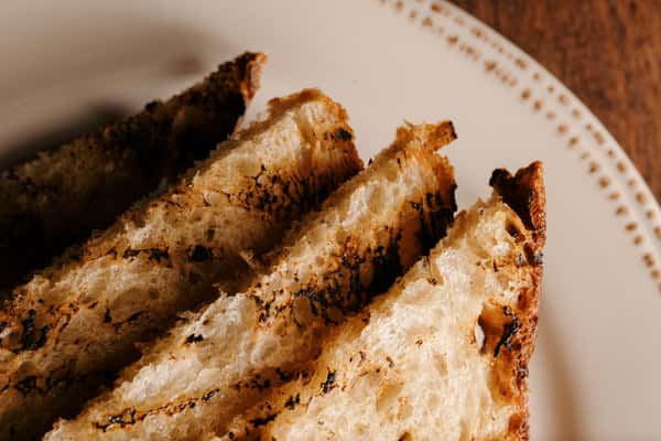 Slices of rustic grilled sourdough bread with charred edges, served on a ceramic plate with a golden, airy crumb texture.