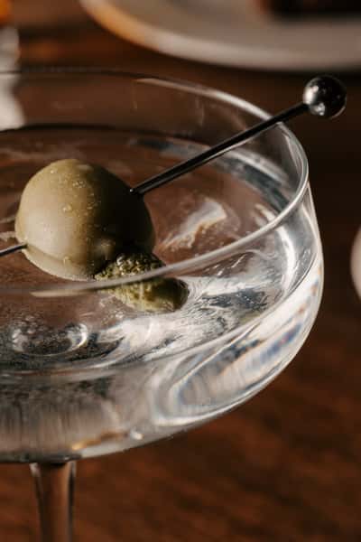 A close-up of a chilled martini garnished with a green olive on a cocktail pick, served in a classic coupe glass.