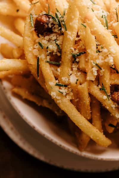 Close-up of crispy truffle fries topped with grated parmesan, chopped rosemary, and garlic, served in a rustic ceramic bowl.