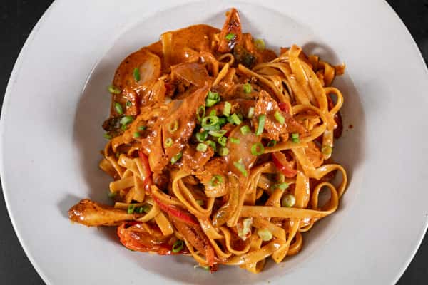 Creamy Cajun chicken fettuccine with sautéed peppers and onions, garnished with chopped scallions in a white bowl.