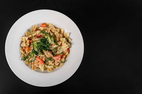 Creamy bowtie pasta with chicken, tomatoes, and broccoli, garnished with fresh basil in a white bowl.