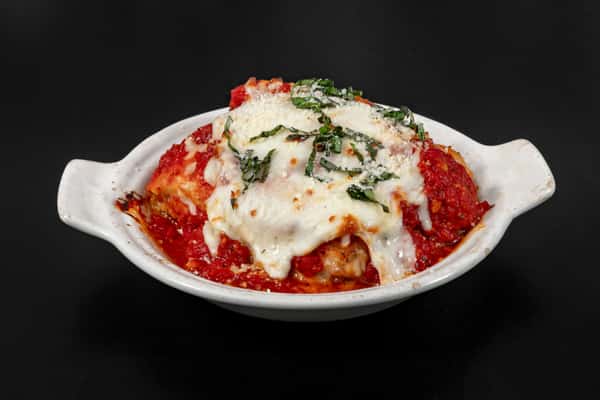 Classic baked lasagna with layers of pasta, marinara sauce, mozzarella cheese, and fresh basil in a white ceramic dish.