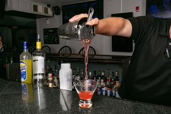 Bartender pouring a pink cocktail from a shaker into a martini glass at a modern bar setup